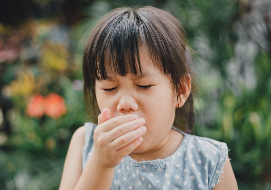 Bé gái đang ho và che miệng, biểu hiện khó chịu ở đường hô hấp