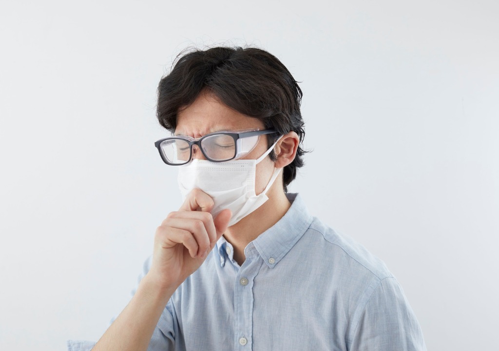 Người đang ho nhẹ từng tiếng, tay chạm vào cổ họng thể hiện cảm giác vướng và kích thích nhẹ.
