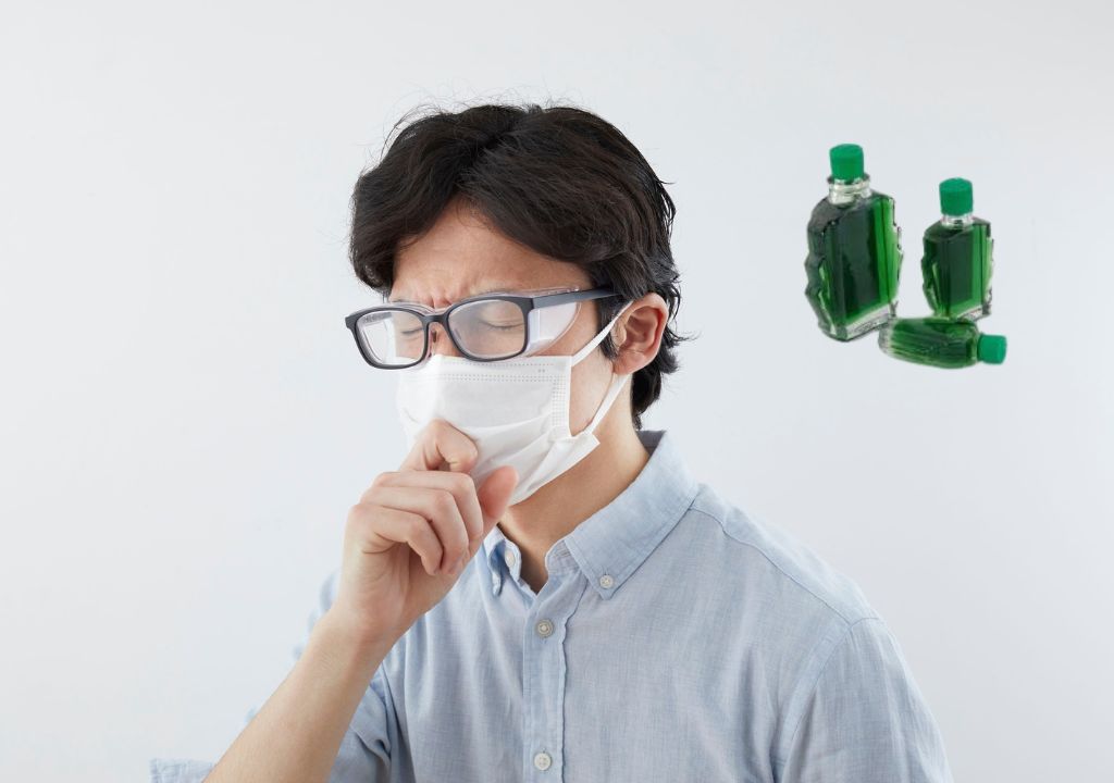 Người đàn ông đeo khẩu trang đang ho, bên cạnh là hình ảnh hai chai dầu gió màu xanh.