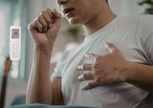 Người đàn ông bị ho khan, tay che miệng và ôm ngực do kích ứng đường hô hấp khi nằm máy lạnh